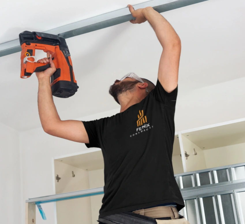 Worker using a nail gun to install trim near a ceiling